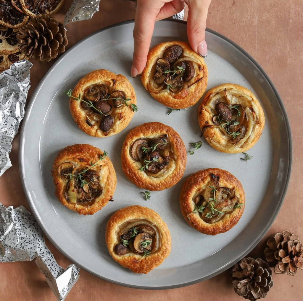 Round puff pastry tartlets topped with sautéed mushrooms and thyme on a gray serving plate.