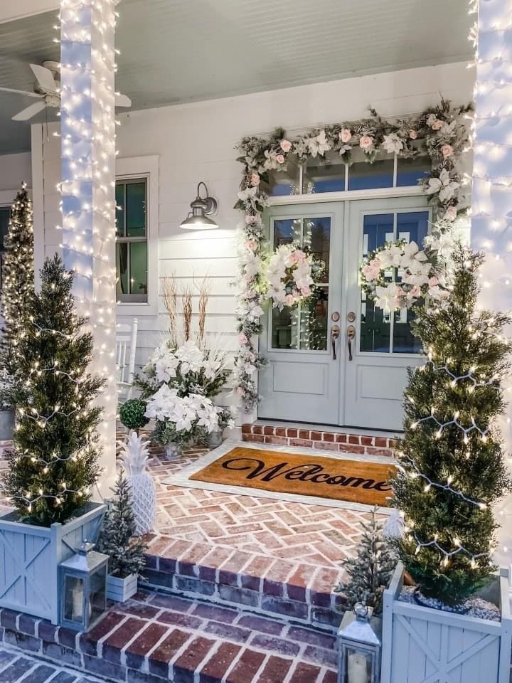 Winter-white porch with blush floral garland, twin wreaths, and light-wrapped columns.