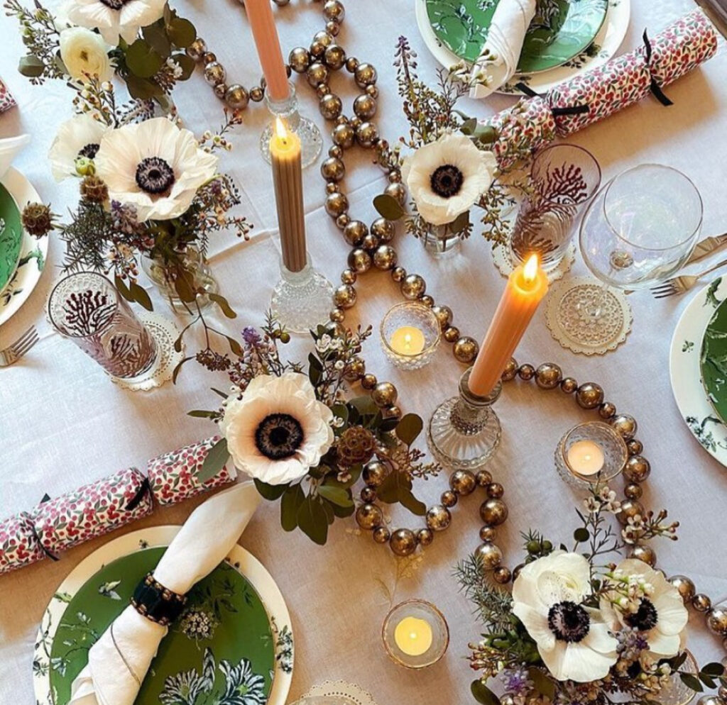 Anemones and bronze bead garland with taper candles on white linen.