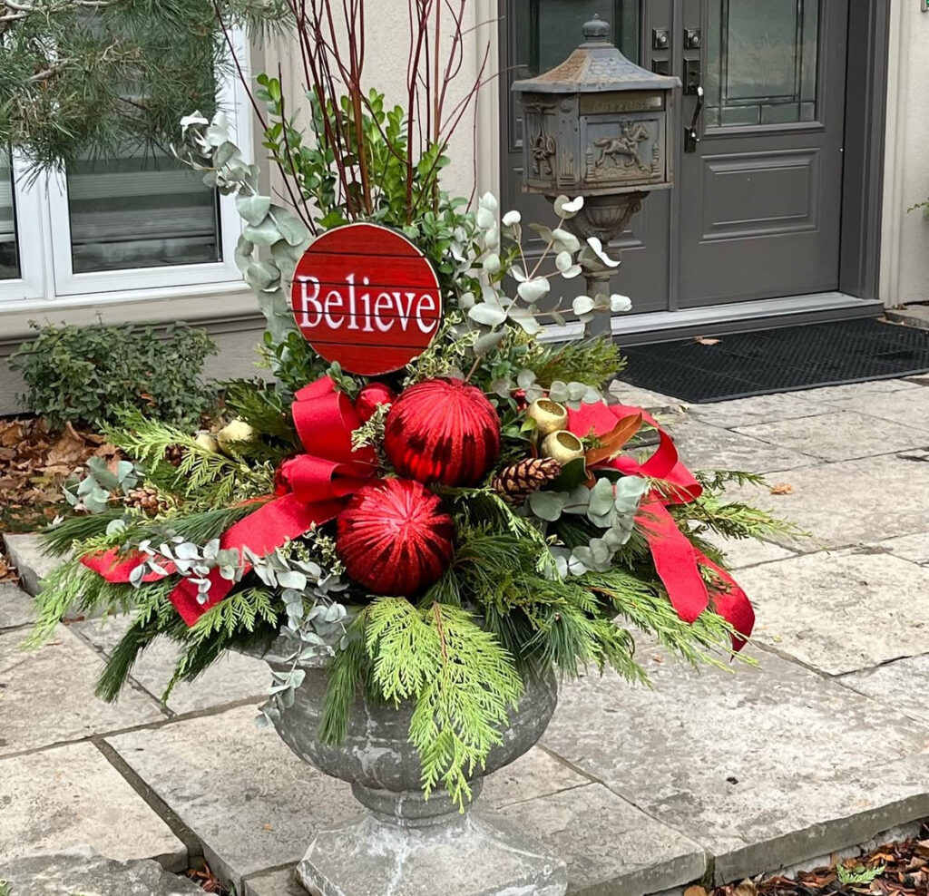 Classic urn layered with cedar, eucalyptus, red dogwood, and a statement ribbon—timeless planter ideas for Christmas for the entry.