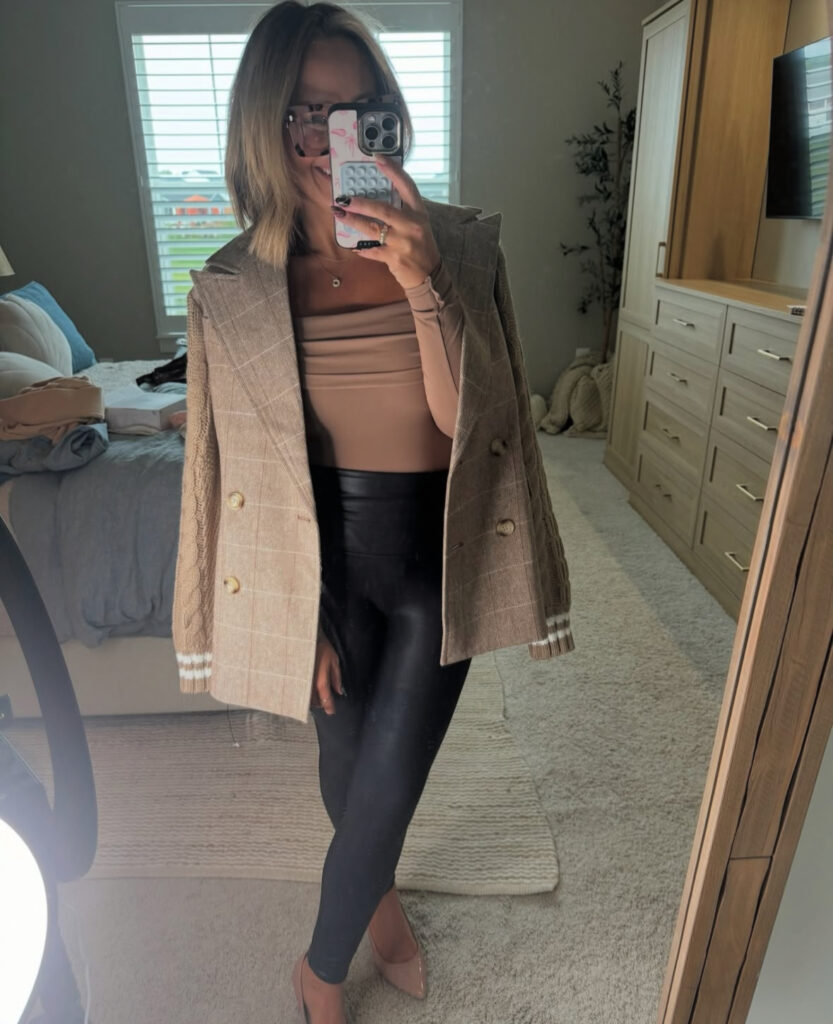 Mirror selfie of nude square-neck top, black faux-leather leggings, taupe plaid blazer draped over shoulders, and nude pointed pumps.