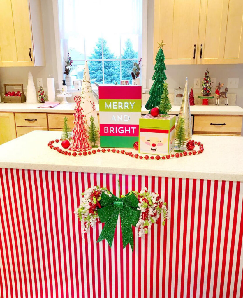 Candy-stripe wrapped island front with “Merry and Bright” signs, cone trees, and red bead garland.