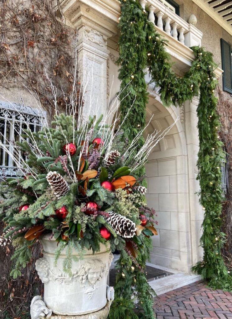 Fir, magnolia, snow-tipped cones, and white branches at a tall doorway—elegant Christmas outdoor winter planter ideas.