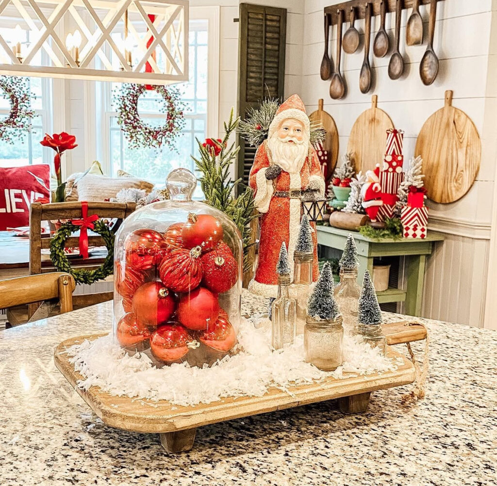 Wooden tray vignette with cloche of red ornaments, Santa figurine, mini trees, and faux snow on island.