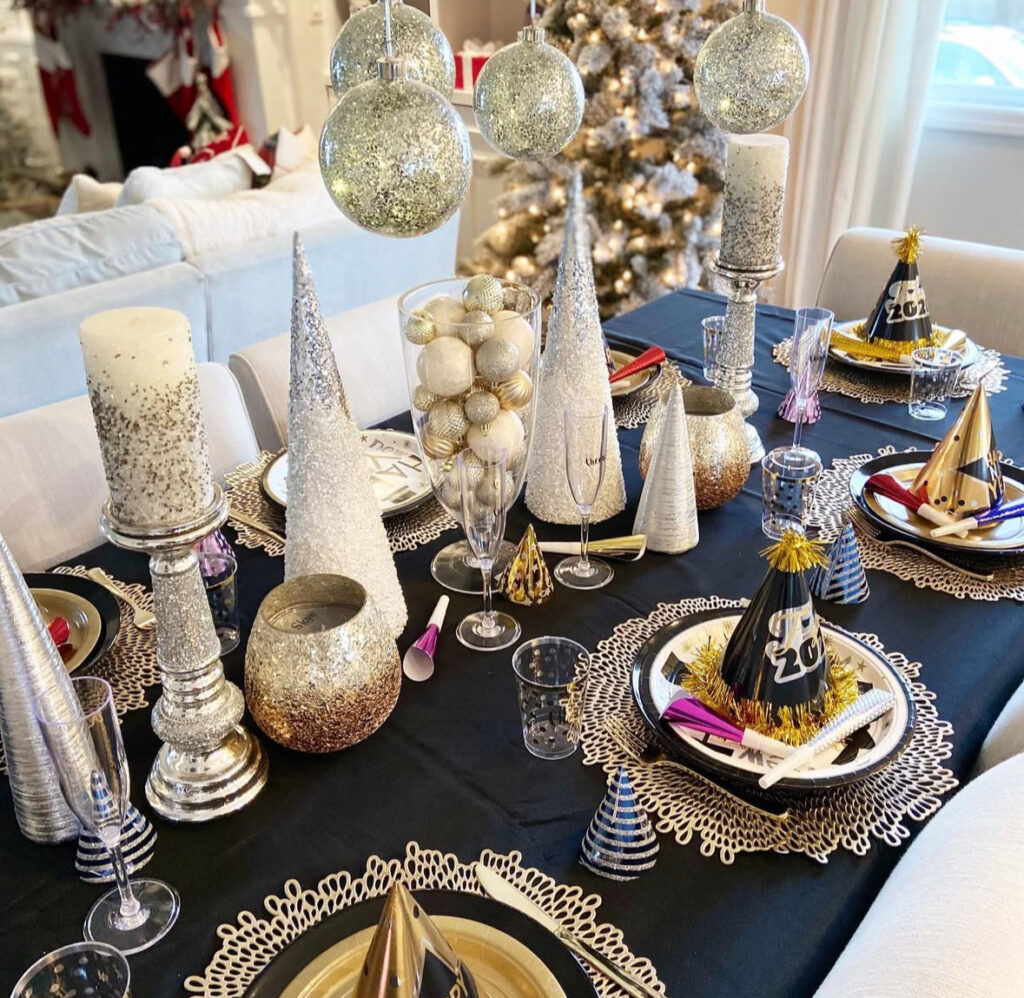 Black table with silver cone trees, hanging glitter ornaments, and hats.