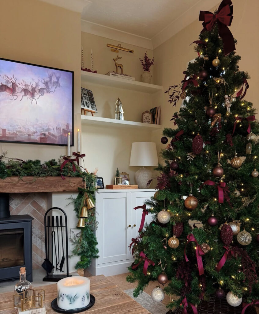 Cozy living room mantel with a burgundy Christmas tree and berry bows