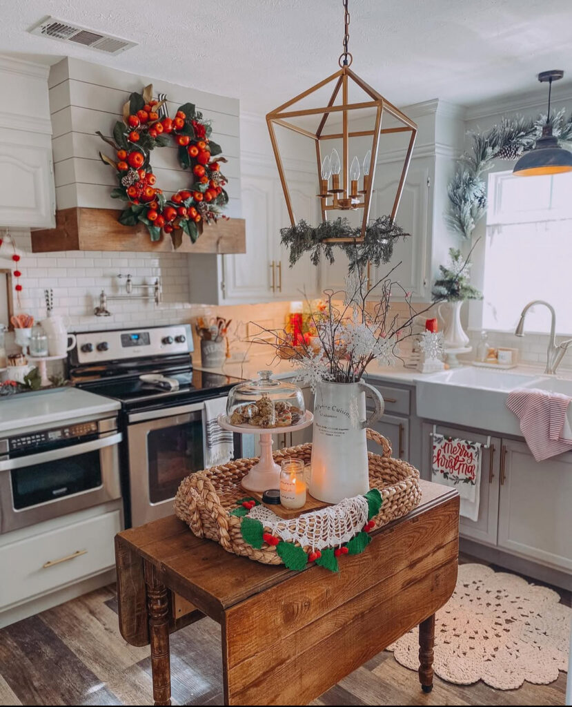Cozy kitchen with apple wreath and small butcher-block island tray holding pitcher, candle, and cloche treats.