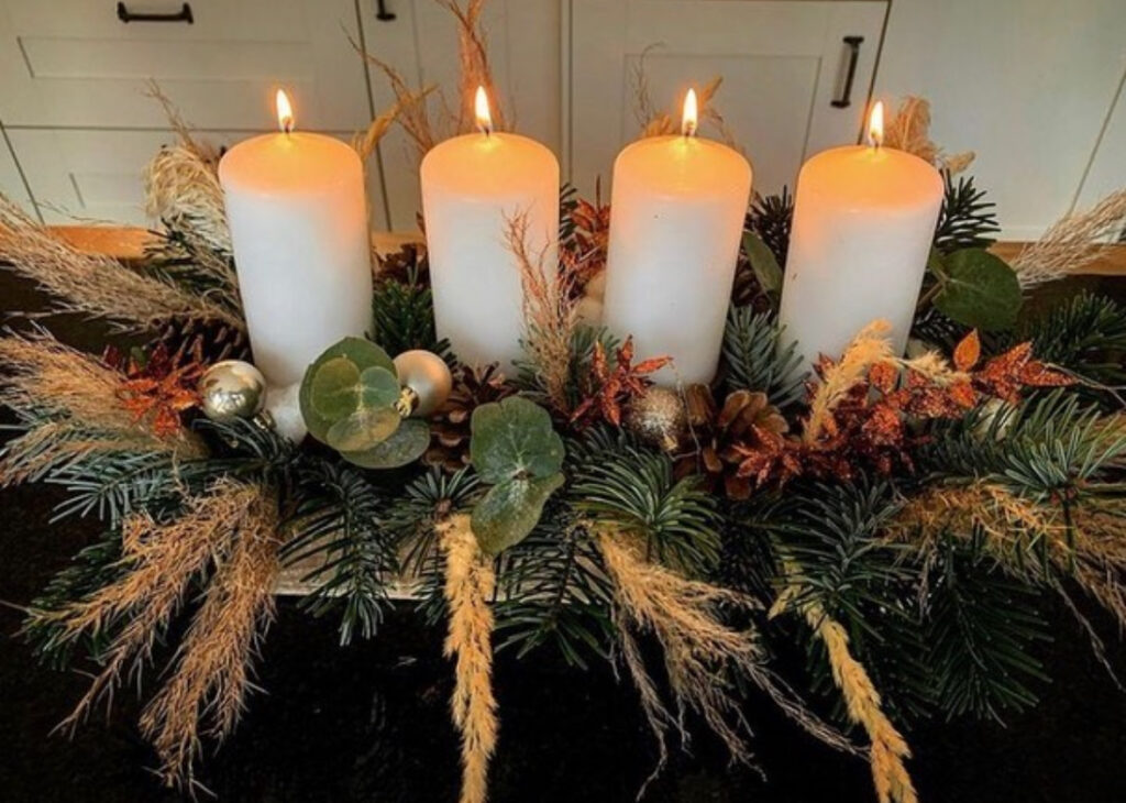 Evergreen arrangement with four white pillar candles as a low kitchen-island centerpiece.