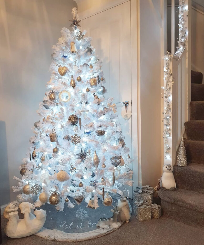 Frosty white christmas tree decorations with silver snowflakes and a cute penguin by the stairs.