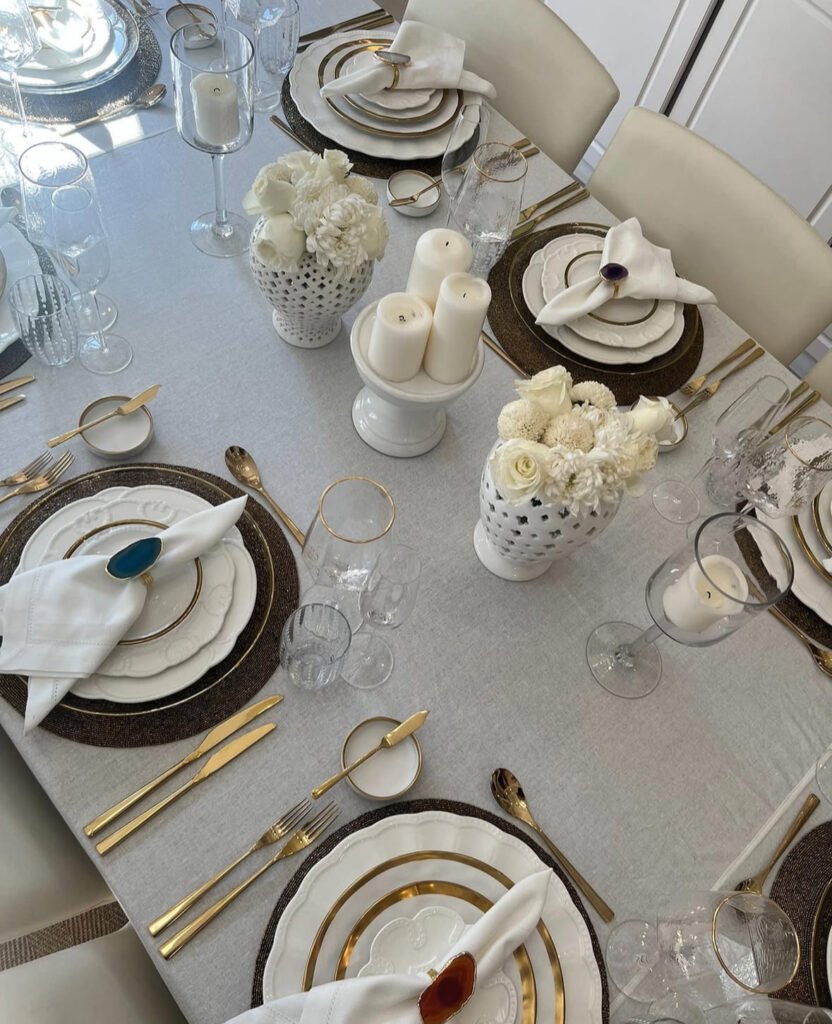 White and gold place settings with gemstone napkin rings and white florals.