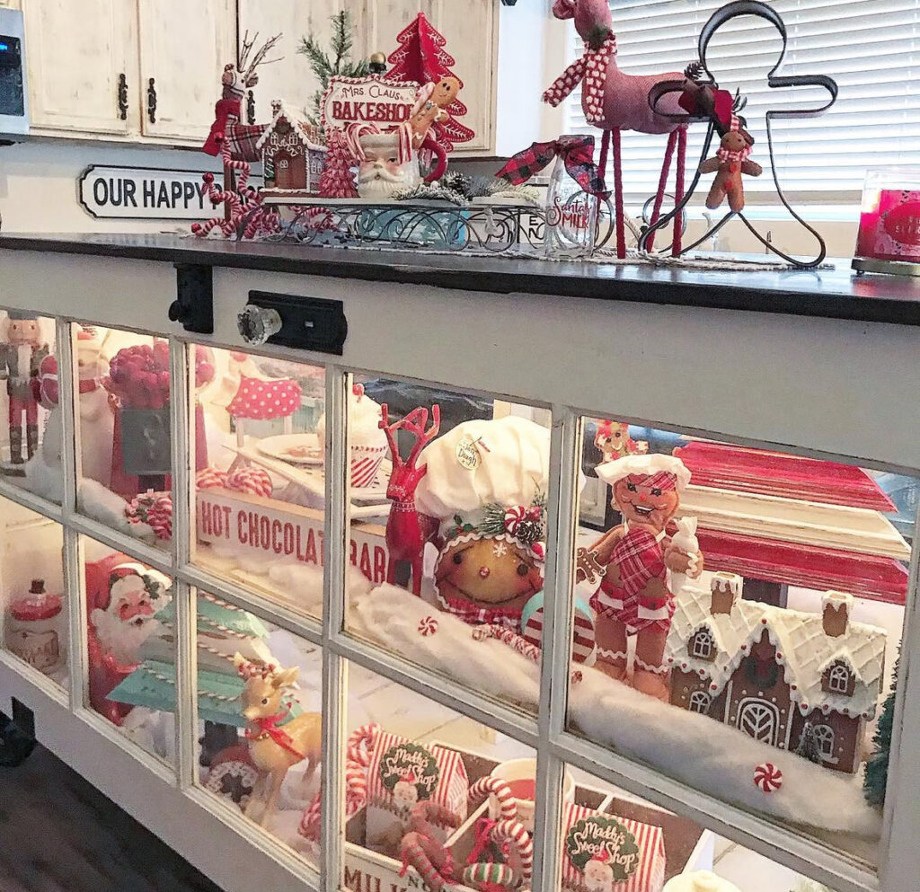 Display island with window-pane cabinets showing gingerbread décor; top tray labeled Mrs. Claus Bakeshop.