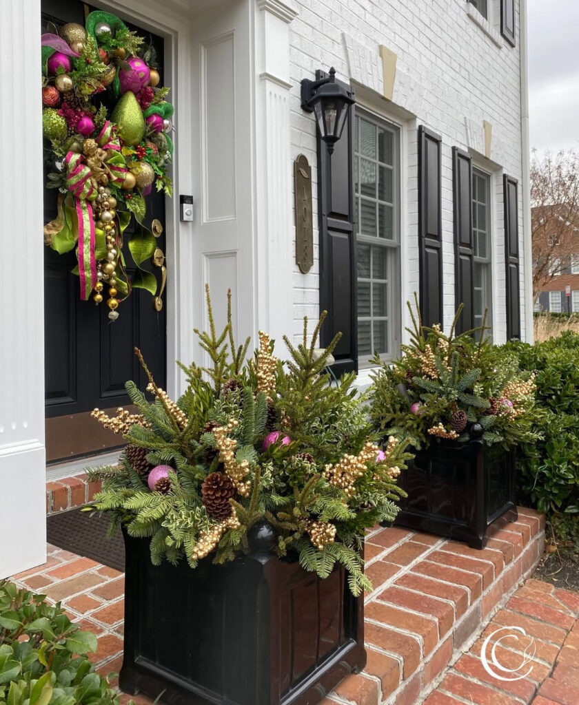 Pair of black cubes with spruce, cones, and gold accents—sleek Christmas outdoor planter ideas for modern entries.