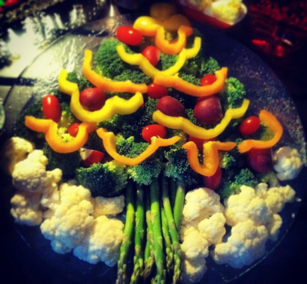 Broccoli tree decorated with yellow pepper swoops and grape tomatoes, asparagus trunk, and cauliflower “snow” along the bottom.