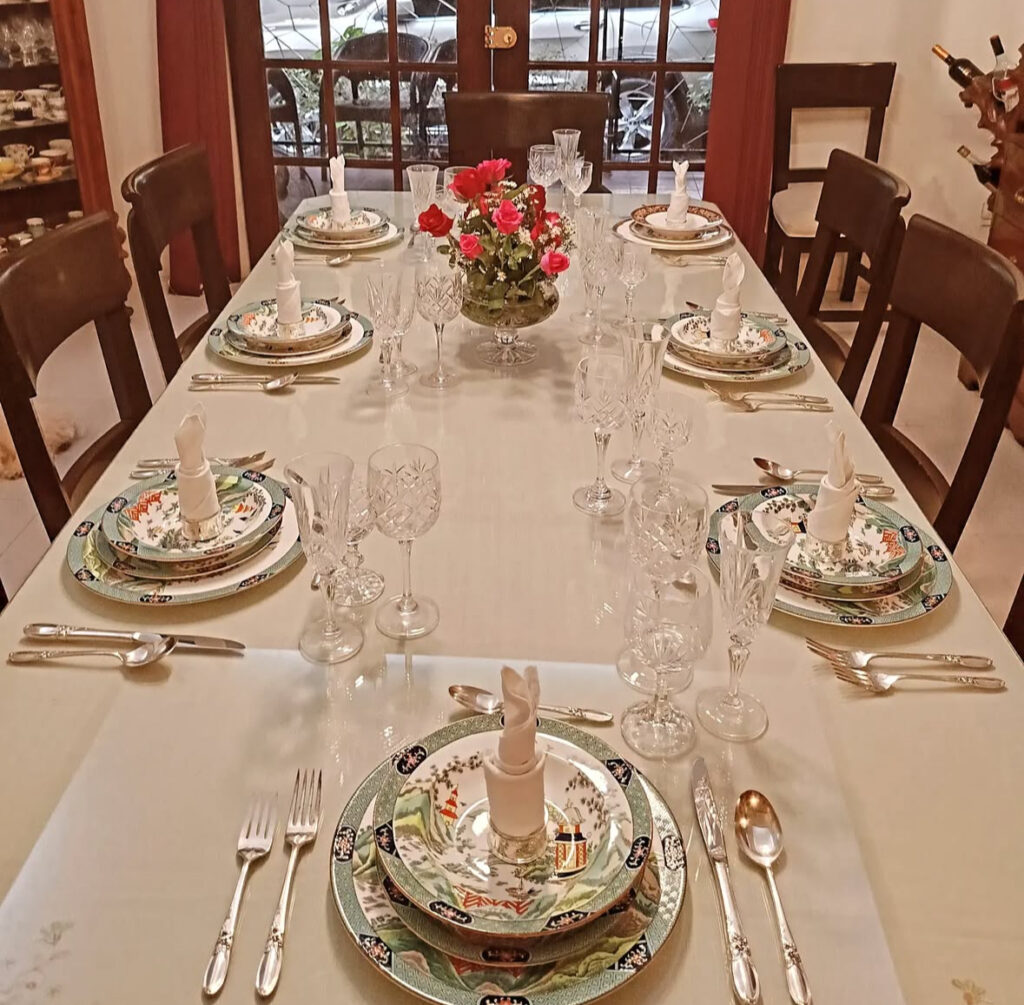 Formal table with crystal stems and patterned plates around rose centerpiece.