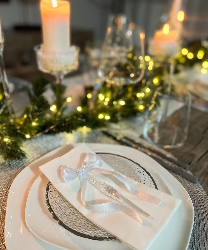 White plate with satin bow and icicle ornament beside twinkle garland.