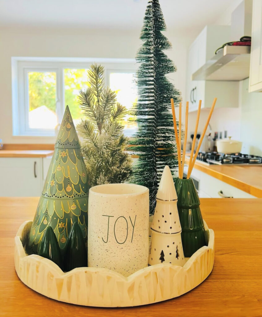 Round tray of ceramic Christmas trees and “JOY” candle on a wood countertop island.