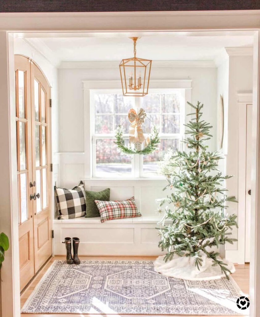 Light filled entryway decorated with a slim Christmas tree and neutral holiday accents
