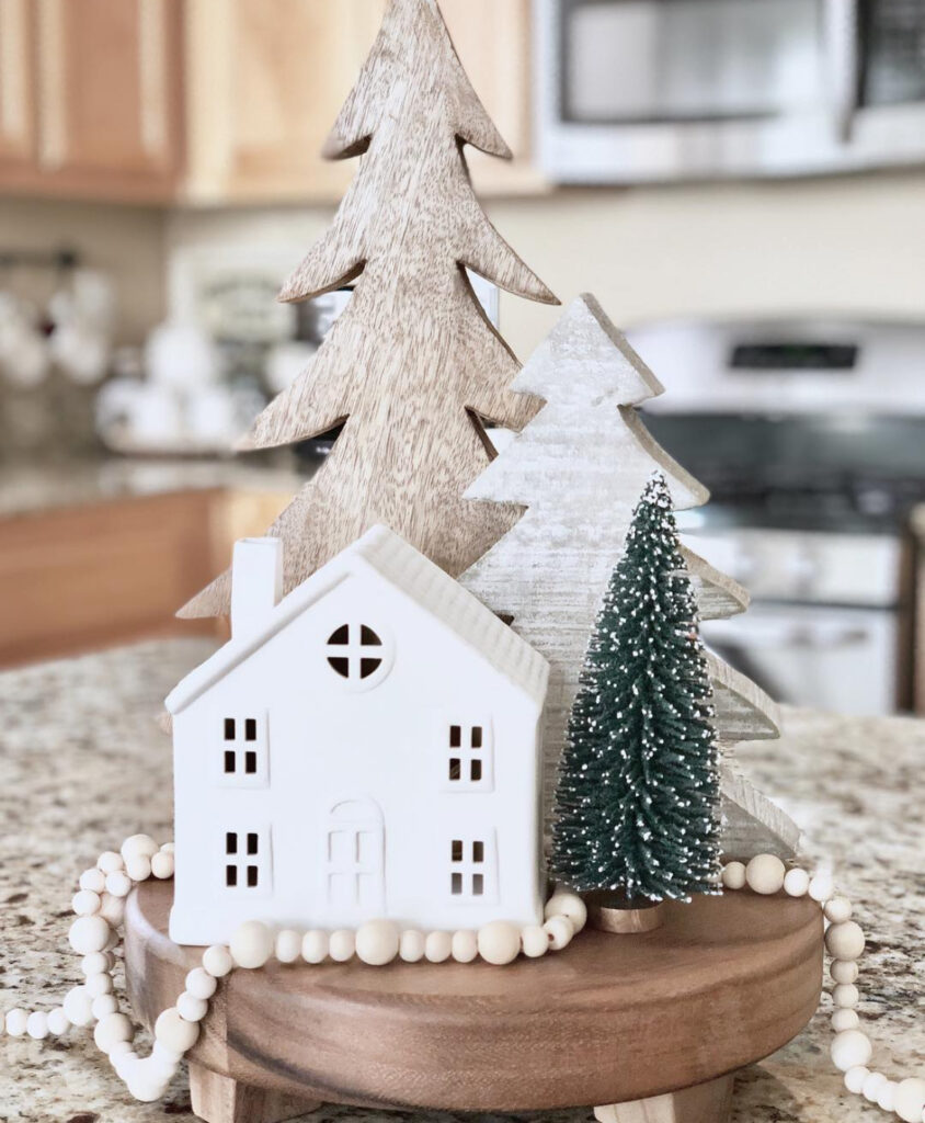 Small wood pedestal on island with white ceramic house, wooden trees, and bead garland.