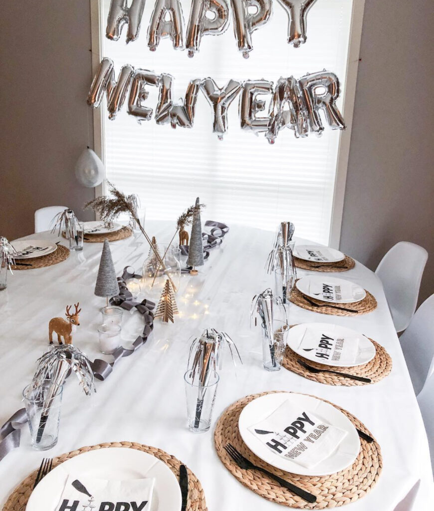 White table under silver “Happy New Year” balloons with woven chargers.