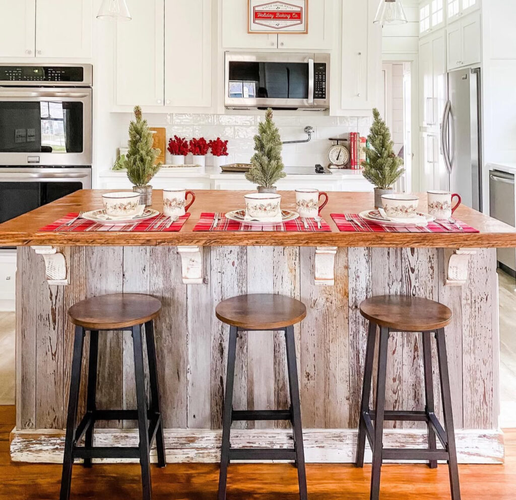 Plaid runners with small potted trees and Christmas mugs set across rustic island.