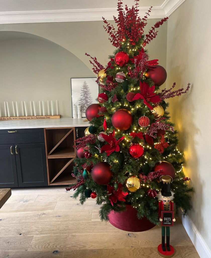 Burgundy Christmas tree with red berries and oversized ornaments beside a nutcracker