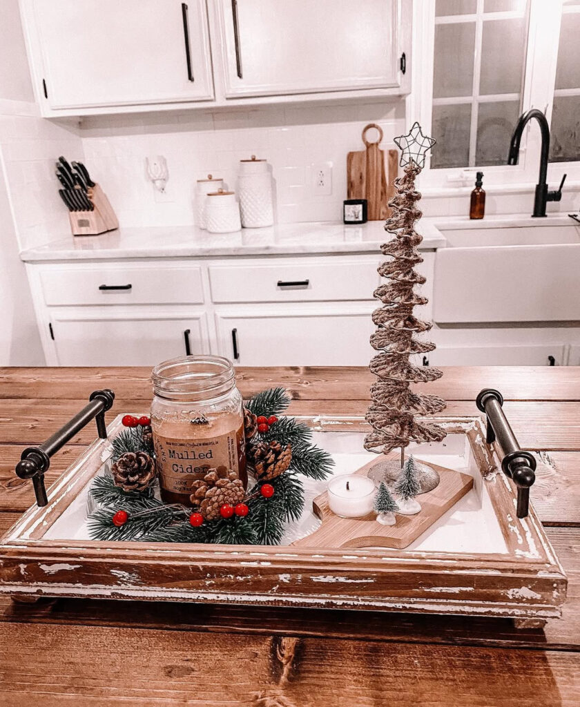 Rustic handled tray with mulled-cider candle in wreath, twig tree, tealight, and mini evergreens on island.