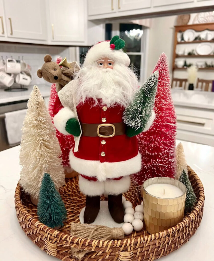 Wicker tray with Santa figure, bottle-brush trees, and candle on a white kitchen island.