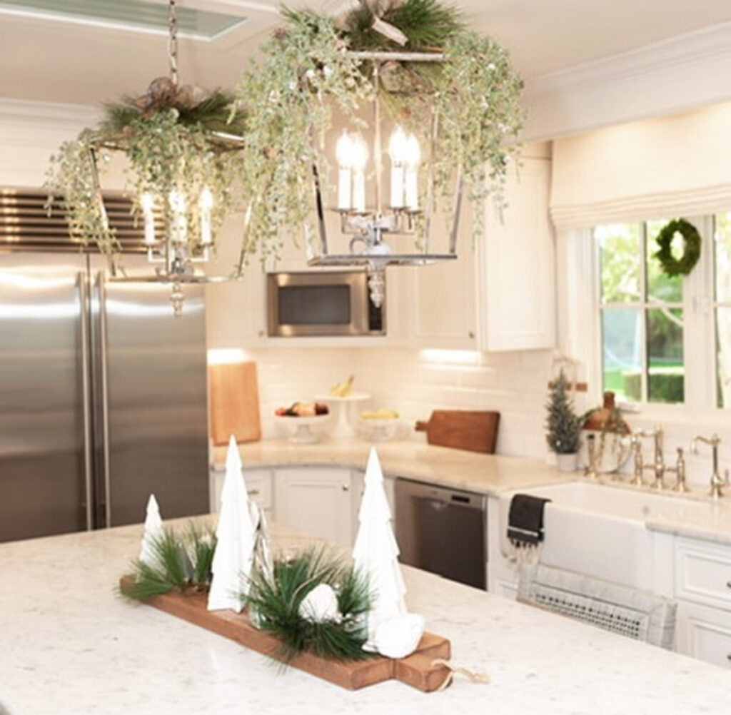 Long wood trough with white ceramic trees and greens on marble island; hanging greenery above.