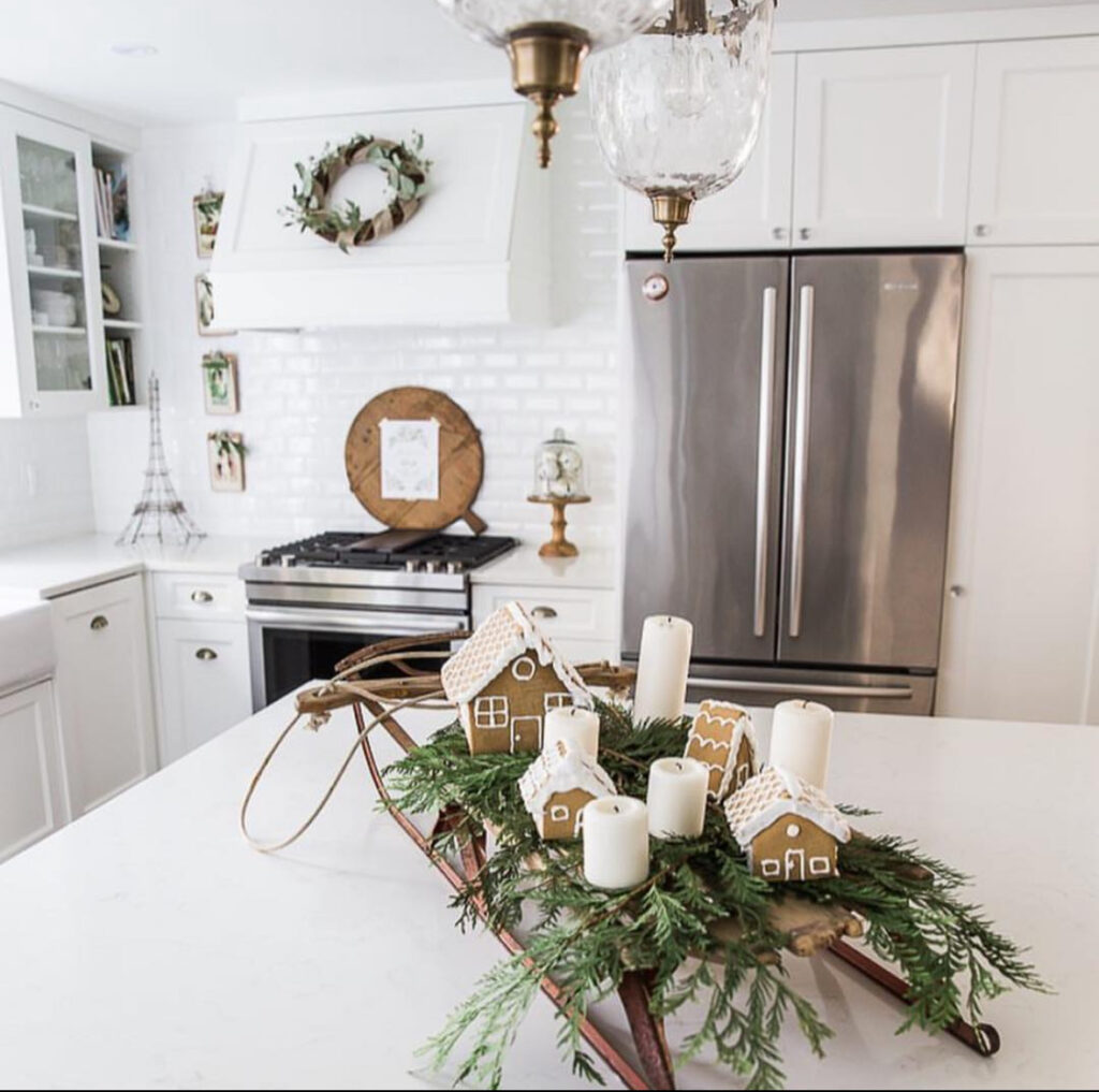 White island centerpiece using vintage sled with greenery, pillar candles, and gingerbread houses.