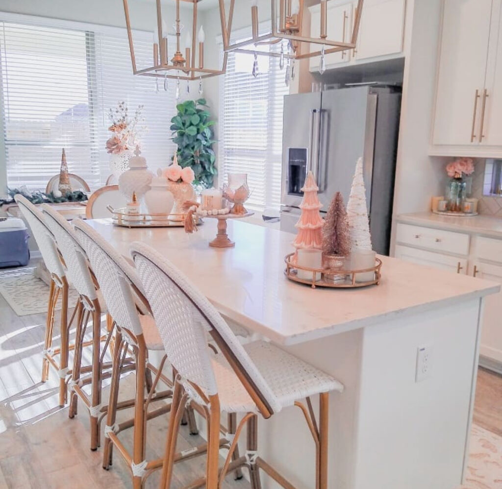 Long bright island styled with blush and white bottle-brush trees, candles, and gold trays; modern lighting.