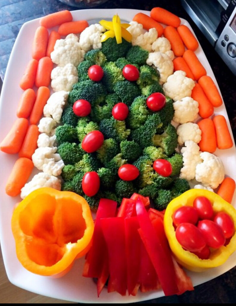 Broccoli Christmas tree platter with cauliflower “snow,” red pepper strips, grape tomatoes, and bell-pepper cups holding tomatoes.