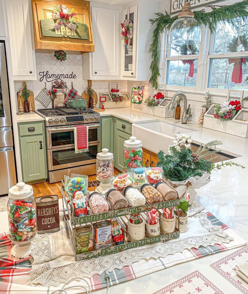 Vintage-style hot cocoa and candy bar on island with jars in a crate; green-and-white kitchen garlanded window.