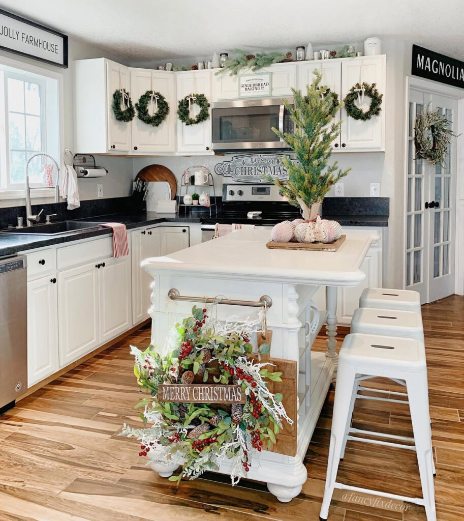 White island with front greenery swag reading “Merry Christmas” and simple tabletop tree; white stools.