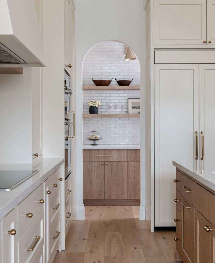 an arched opening at the end of the kitchen reveals white tile walls and floating walk in pantry shelves above a small cabinet