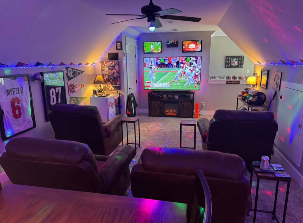 Multiple screens, recliners, and team memorabilia showcase colorful sports man cave ideas in a sloped attic room.