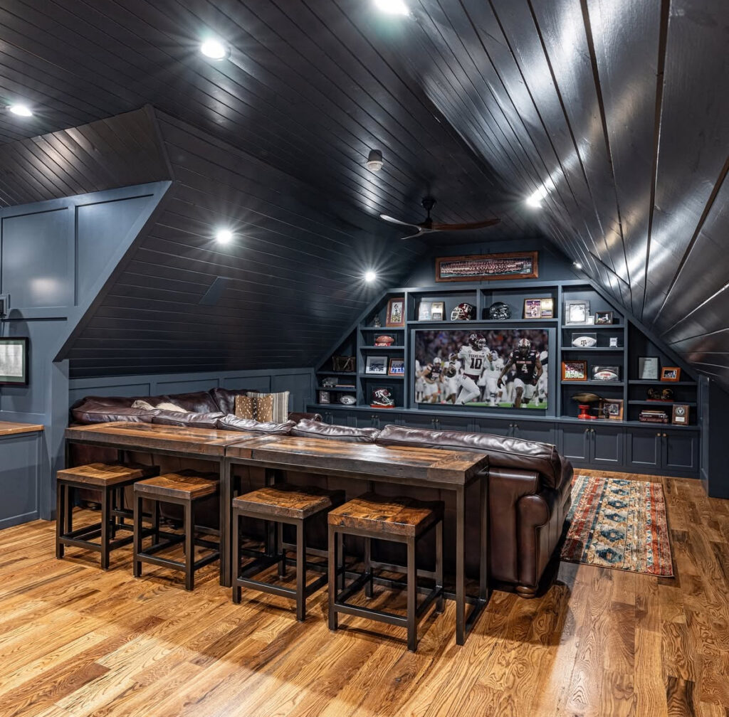 Tiered seating, a long bar table, and built-in shelves packed with memorabilia are smart basement man cave ideas for movie and game nights.