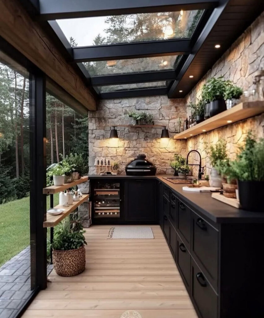 Glass-roofed room with stone walls, black cabinets, and herb shelves forming an immersive outdoor kitchen layout