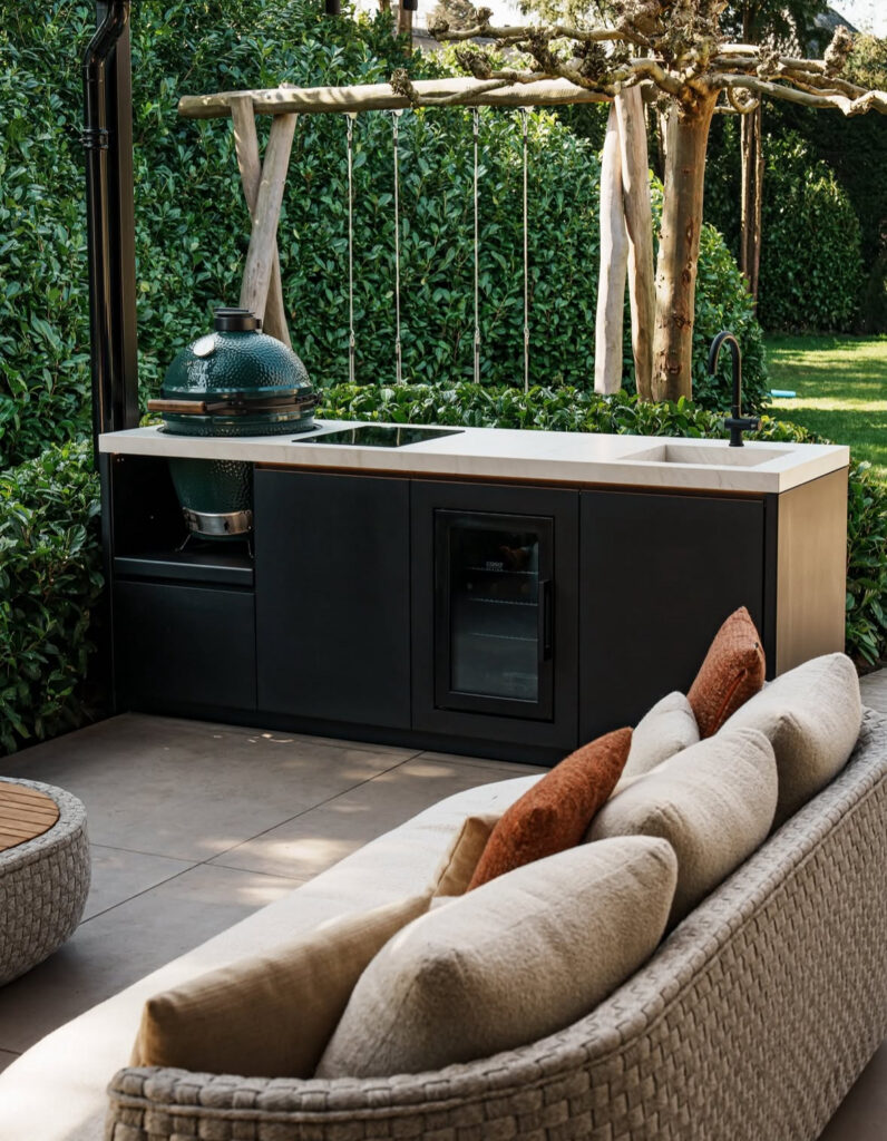 Low black cabinet run with kamado grill beside an outdoor sofa giving relaxed backyard outdoor kitchen ideas