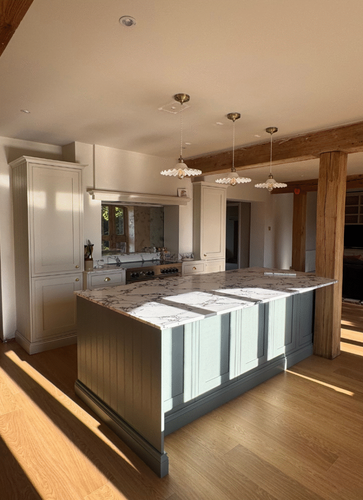 Light-filled country kitchen with exposed beams, marble island, and sage cabinetry, showcasing elegant barn conversion ideas.
