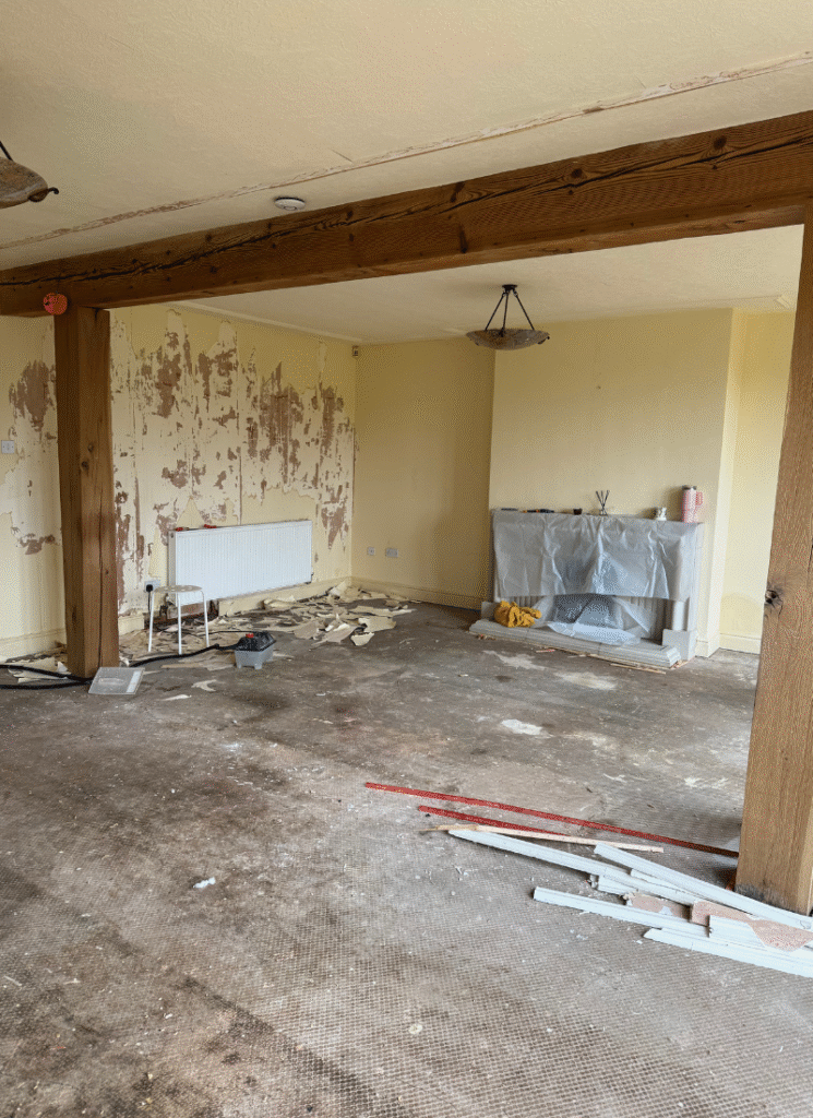 Stripped-back living room with exposed subfloor, beams, and a covered fireplace, revealing the raw starting point for future barn conversion ideas.