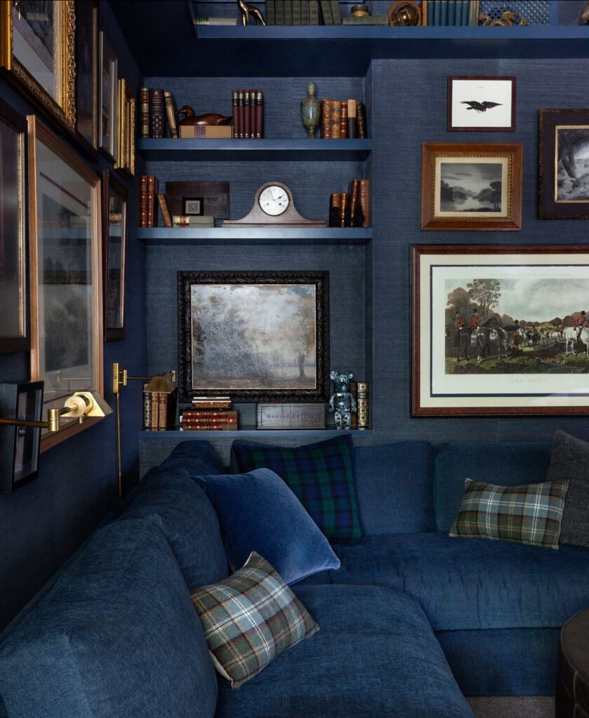 A deep blue sectional, plaid pillows, and book-filled shelves offer cozy small man cave ideas for a reading nook.