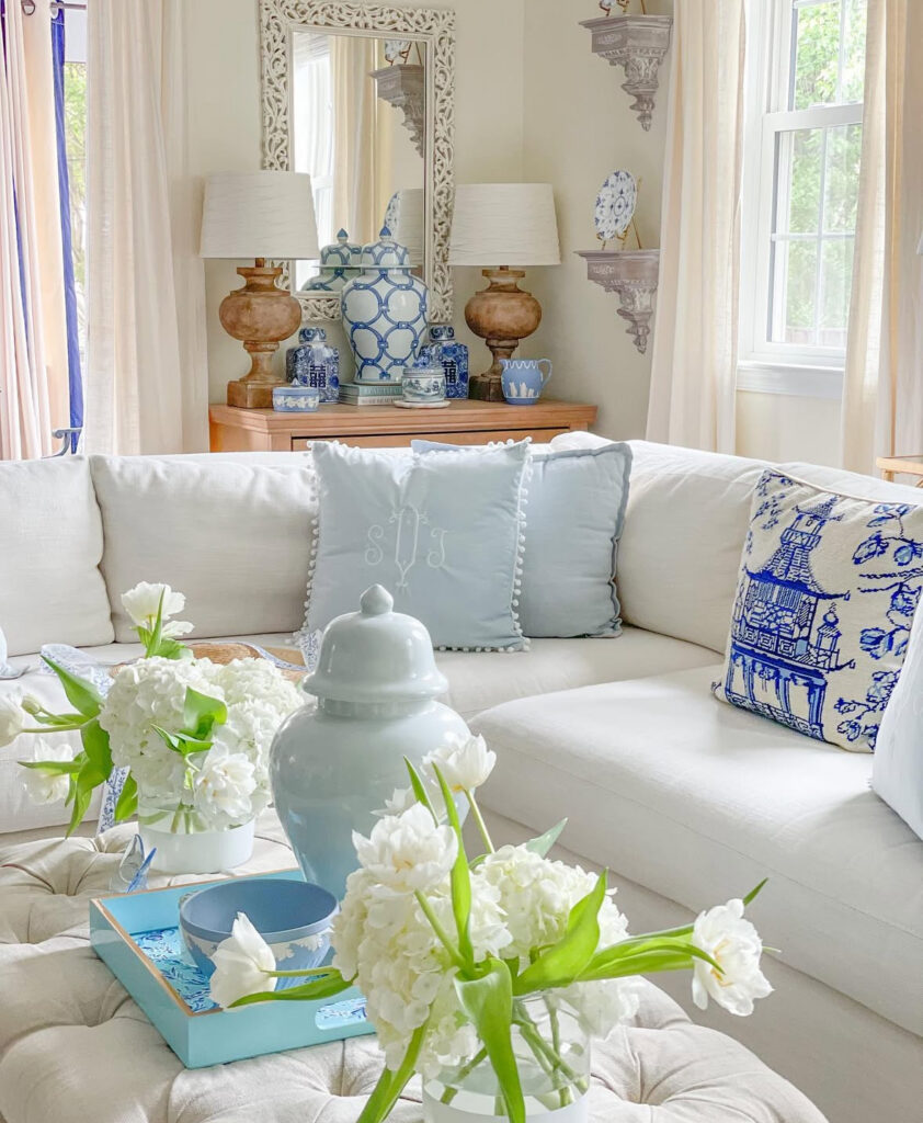 A white sectional with soft blue pillows and ginger jars on a console creates a bright, cozy french country living room.