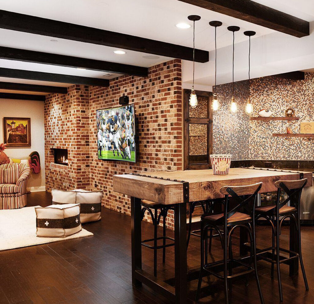 Exposed brick, a big TV, and bar-height seating turn this room into classic sports man cave ideas for game-day hosting.