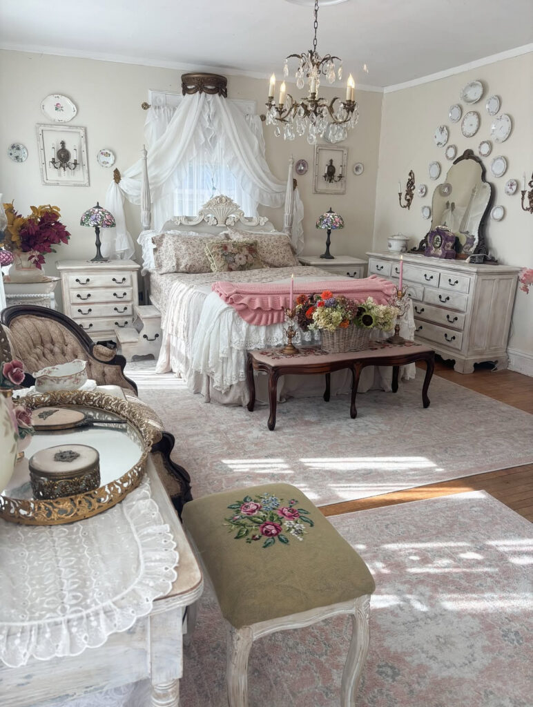 Canopy bed, crystal chandelier, and vintage dressers creating classic shabby chic bedroom decor.