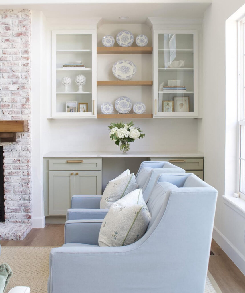 Powder-blue armchairs face cabinetry displaying blue-and-white china in a subtly rustic french country living room nook.