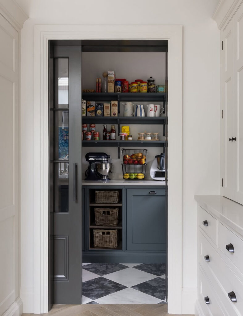 sliding door reveals a compact walk in pantry with countertop space for appliances wicker baskets and open shelving