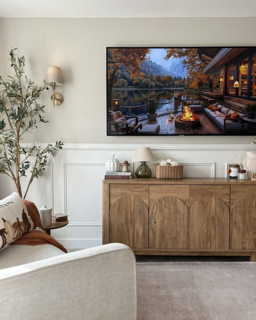 Neutral cottage living room with wainscoting, warm wood console, and landscape image on the screen providing relaxed tv wall ideas for living room areas with classic trim.