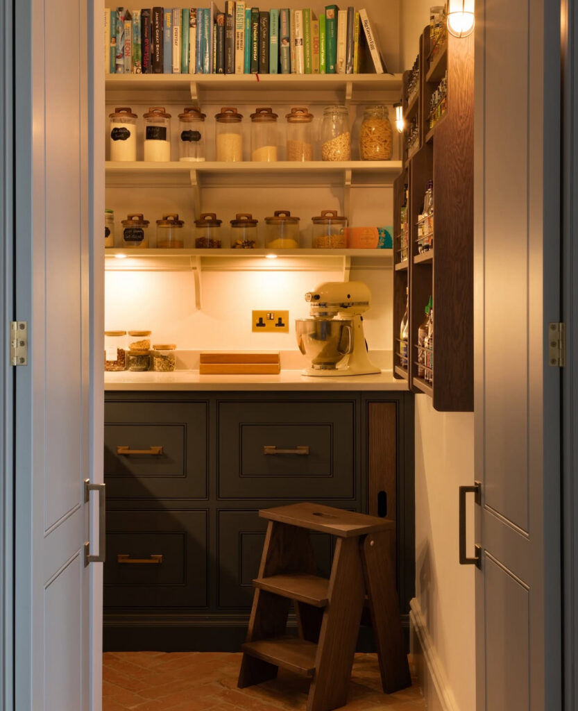 warmly lit pantry with cookbooks labeled jars a stand mixer and step stool forms a cozy baker focused kitchen pantry