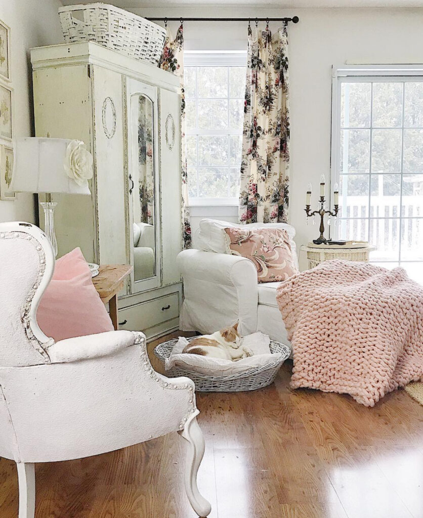 Soft white armchair, floral curtains, and chunky knit blanket creating cozy shabby chic bedroom decor.