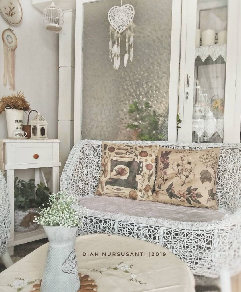 Cozy wicker loveseat corner with lace details and shabby chic bird cage decor on the wall.